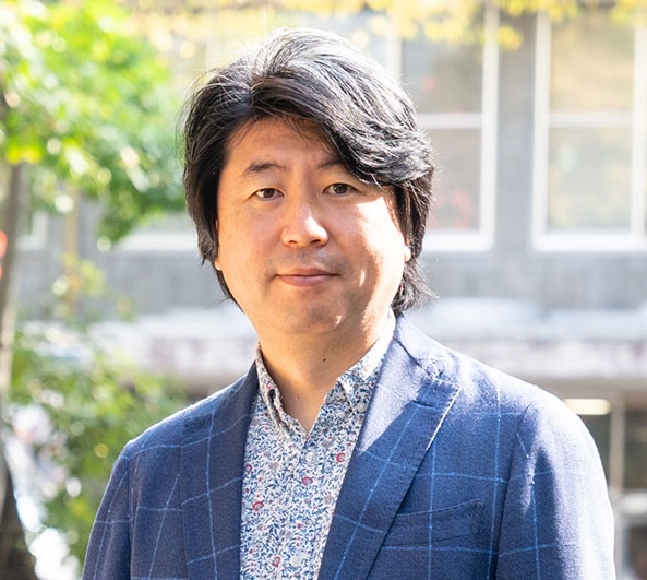 伊藤達矢さんの顔写真。濃い髪の男性で、紺色のチェック柄のジャケットを着て、屋外で静かに微笑んでいる