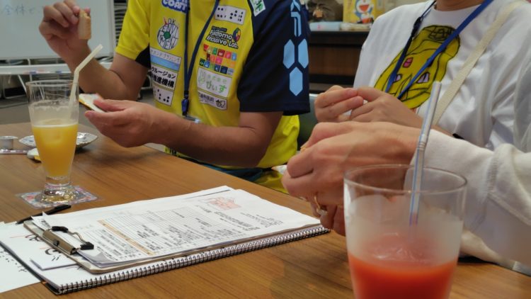 コーヒーやジュースが置かれているテーブルで参加者それぞれが展覧会の感想について話している写真。