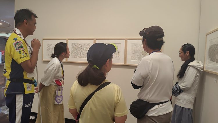 タスキをかけた駅伝ランナーが描かれた絵画の前で話している写真。絵を鑑賞している5名中3名は、走りやすい運動着の服装で写っている。