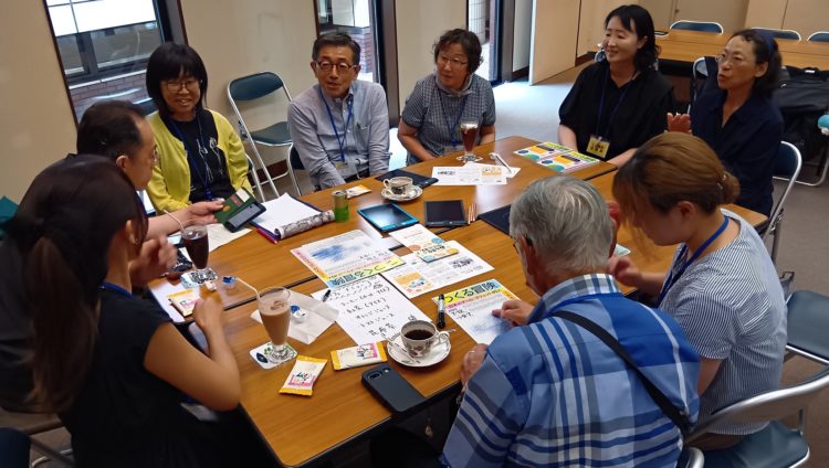 手話通訳を含めた9名がテーブルを囲んでお茶やジュースを飲みながら展覧会の感想について話している写真。デバイスや筆談を使いながらコミュニケーションを取っている。