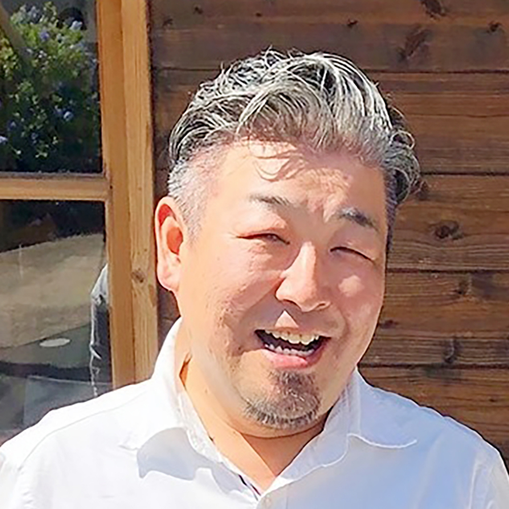 樋口 龍二さんの顔写真。白い色のシャツを着用し、日差しが強い屋外で目を細めて微笑んでいる