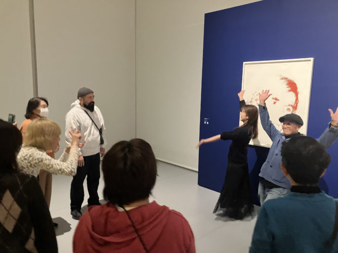 人物肖像画の前に集まった参加者が腕を上げたり身振りを交え、感じたことを表現している様子の写真