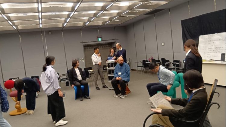 研修会の会場に並べられた色とりどりで様々な形のデザイン椅子に参加者が腰を掛け、座り心地を確かめながら対話している様子の写真。