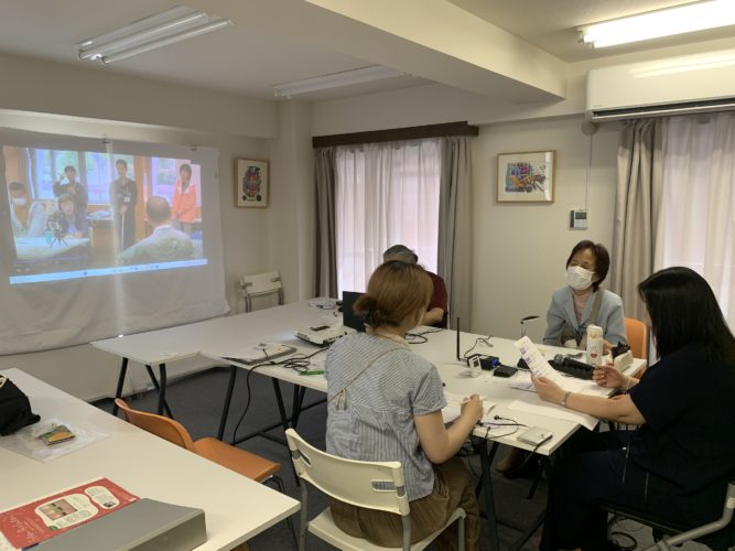 音声ガイドのクオリティチェック会議中の写真。事務所の机を囲んでナレーションの内容を話し合っている。